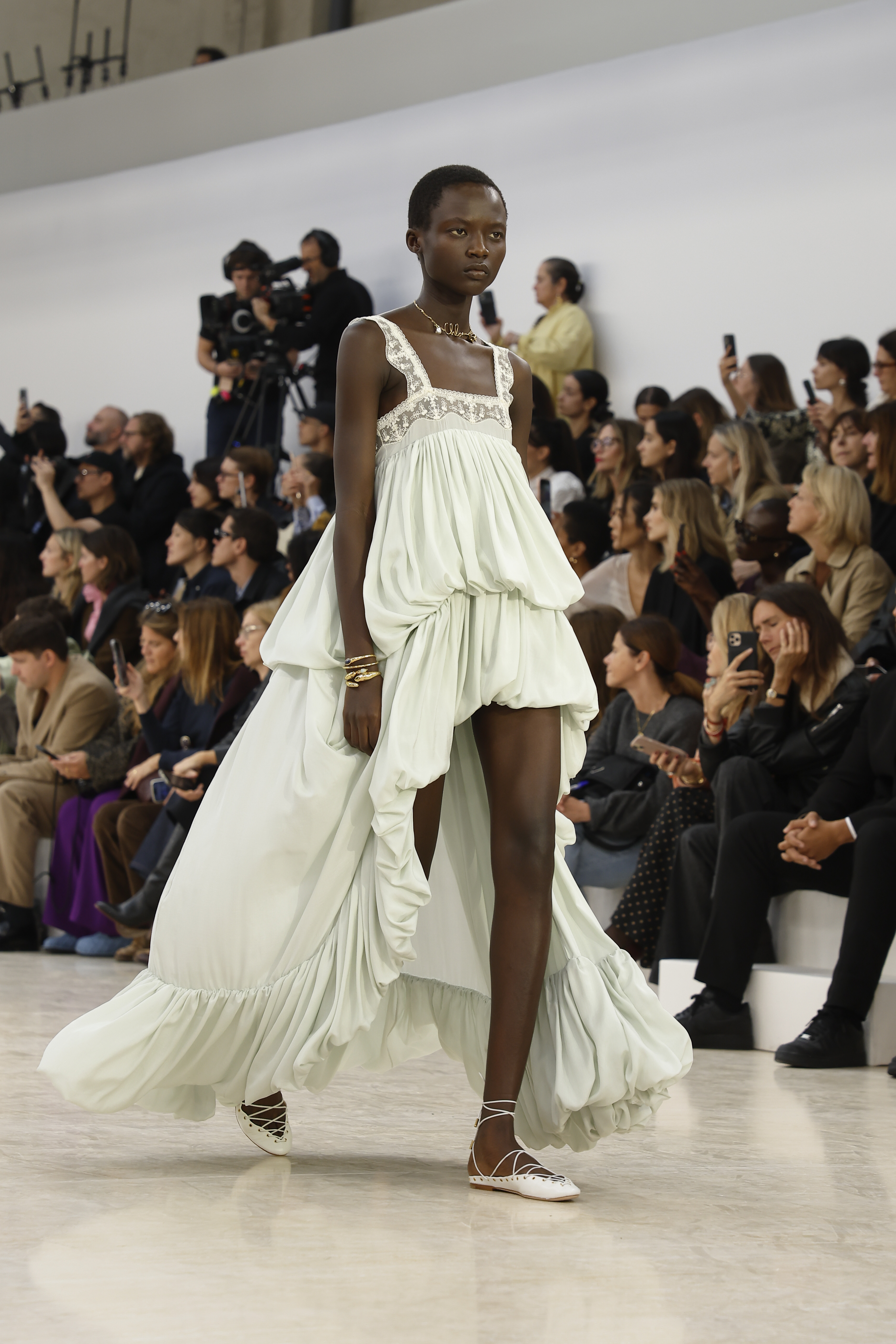 A model wears a green gown and white lace-up shoes on the Chloé runway