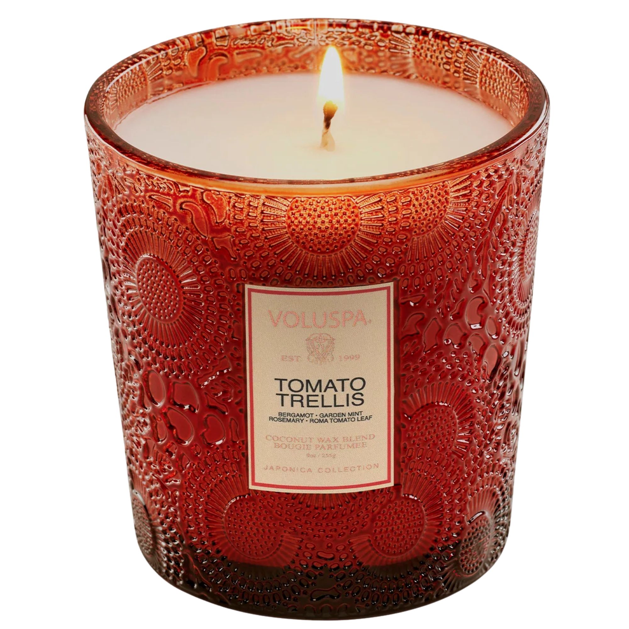 A lit Voluspa tomato trellis candle in a red glass vessel