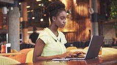 A woman sitting at a table and using a laptop with her phone nearby