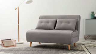 A small sofa bed upholstered in grey velvet in a modern living room