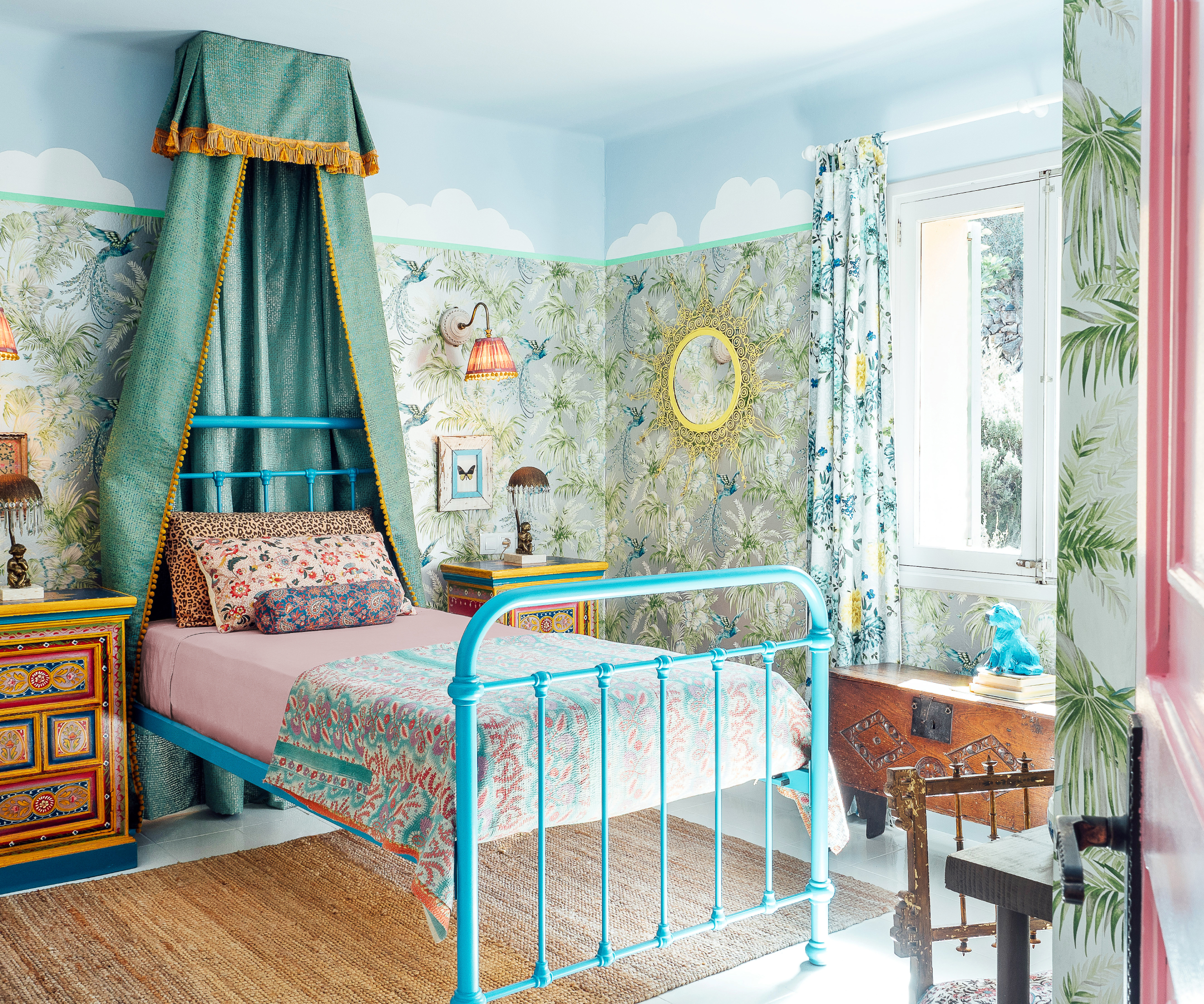 bedroom with turquoise bed and canopy, floral patterned wallpaper and cloudscape above picture rail