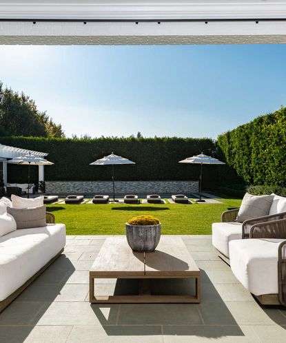 An example of south facing garden ideas showing a large garden with three white parasols and a patio area with outdoor sofas