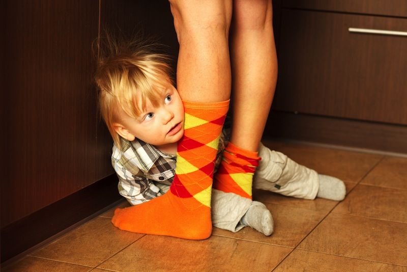 Shy toddler hiding behind mom&#039;s legs