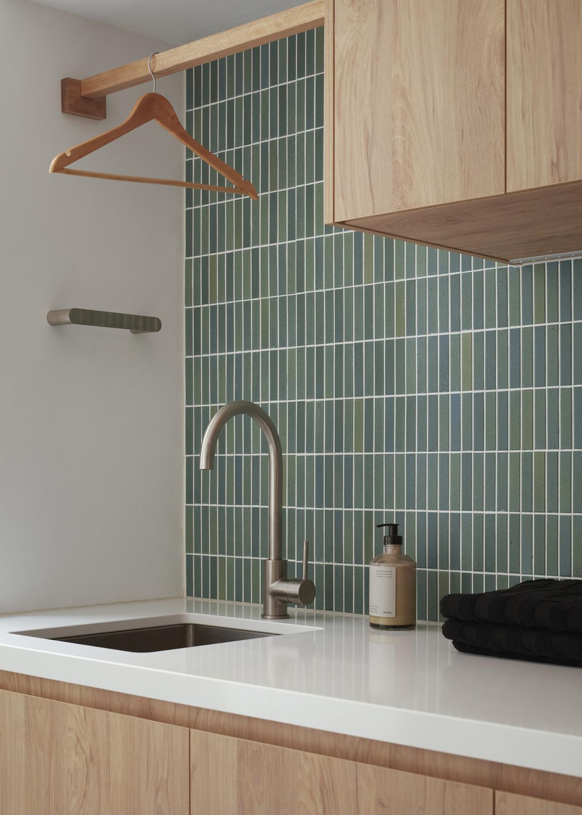 A laundry room with a rail for hanging clothes, a sink, and a folded towel by a bottle of soap