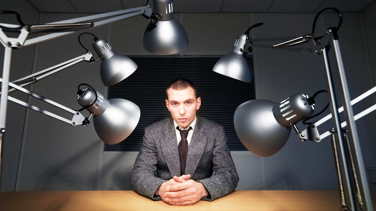 A man sits under interrogation lights.