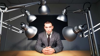 A man sits under interrogation lights.