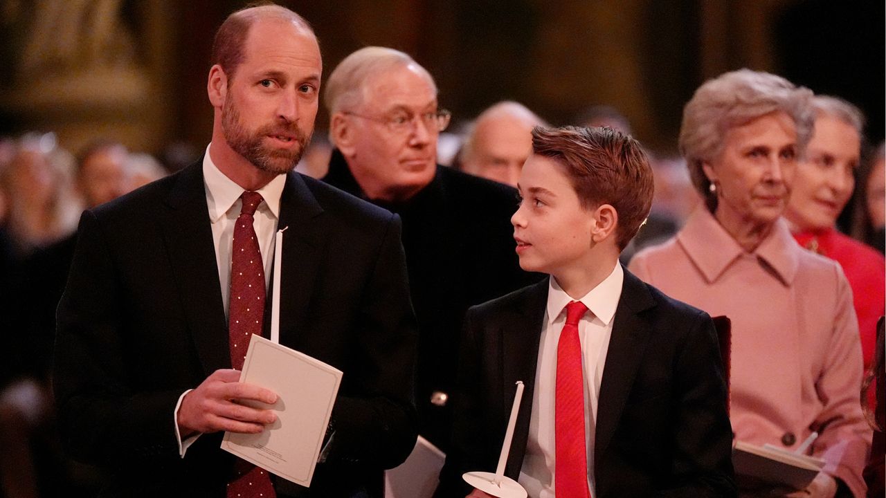 Prince William and Prince George wearing suits and red ties holding candles at a church service and looking at each other