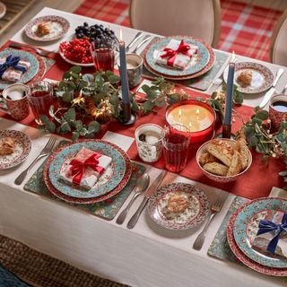 Festive table setting with red runner, candles and placemats with fancy dinnerware