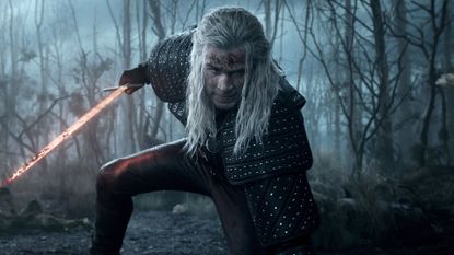 Liam Hemsworth kneels on one knee while holding a sword 