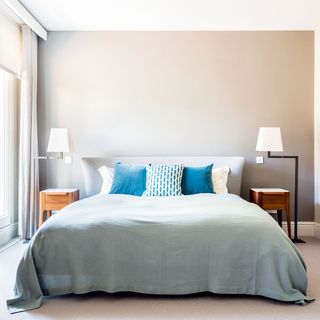 Grey bedroom with blue pillows on top of a bed with bedside tables and lamps