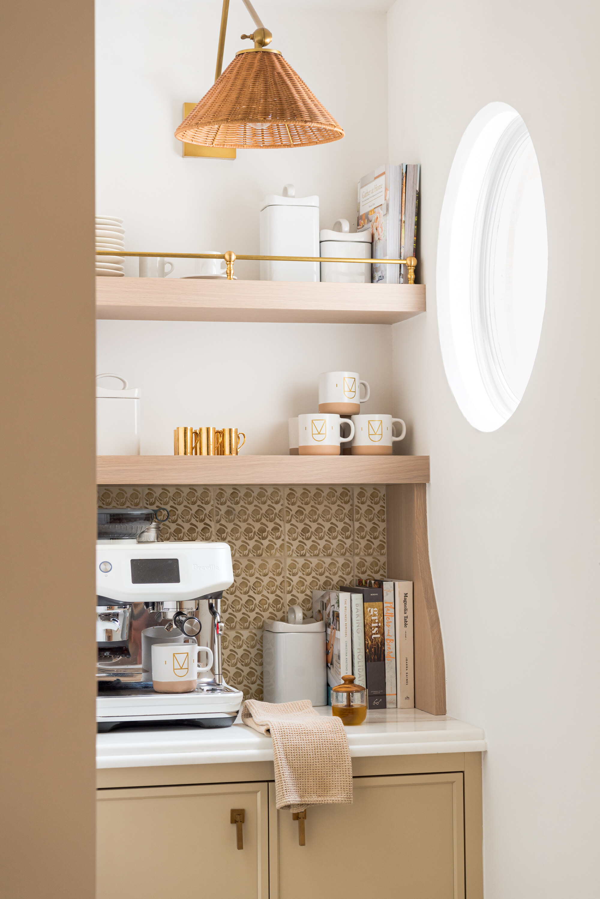 Image of a bright coffee station. There are wooden shelves with coffee mugs and storage tins, and a white marble countertop that has a large, white espresso machine on it.