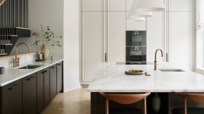 a black and white kitchen with uncluttered countertops and a large island. a sink on one side, with a brass tap, is open onto the stairs