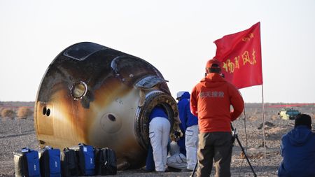 a scorched cone-shaped capsule lies on a desert floor surrounded by people in thick blue coats