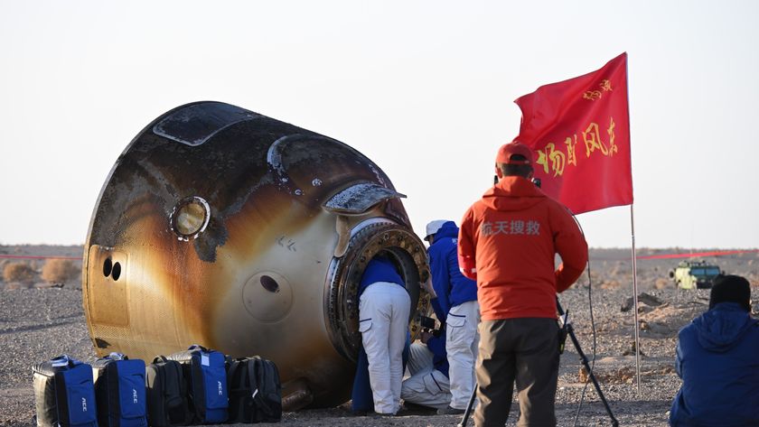 a scorched cone-shaped capsule lies on a desert floor surrounded by people in thick blue coats