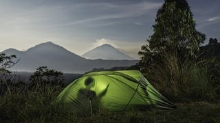 Woman inside tent using digital tablet, under moonlight, in front of mount agung