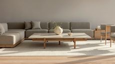 A Scandi living room with a neutral palette, featuring a cream rug, a low profile coffee table, and grey sectional sofa 