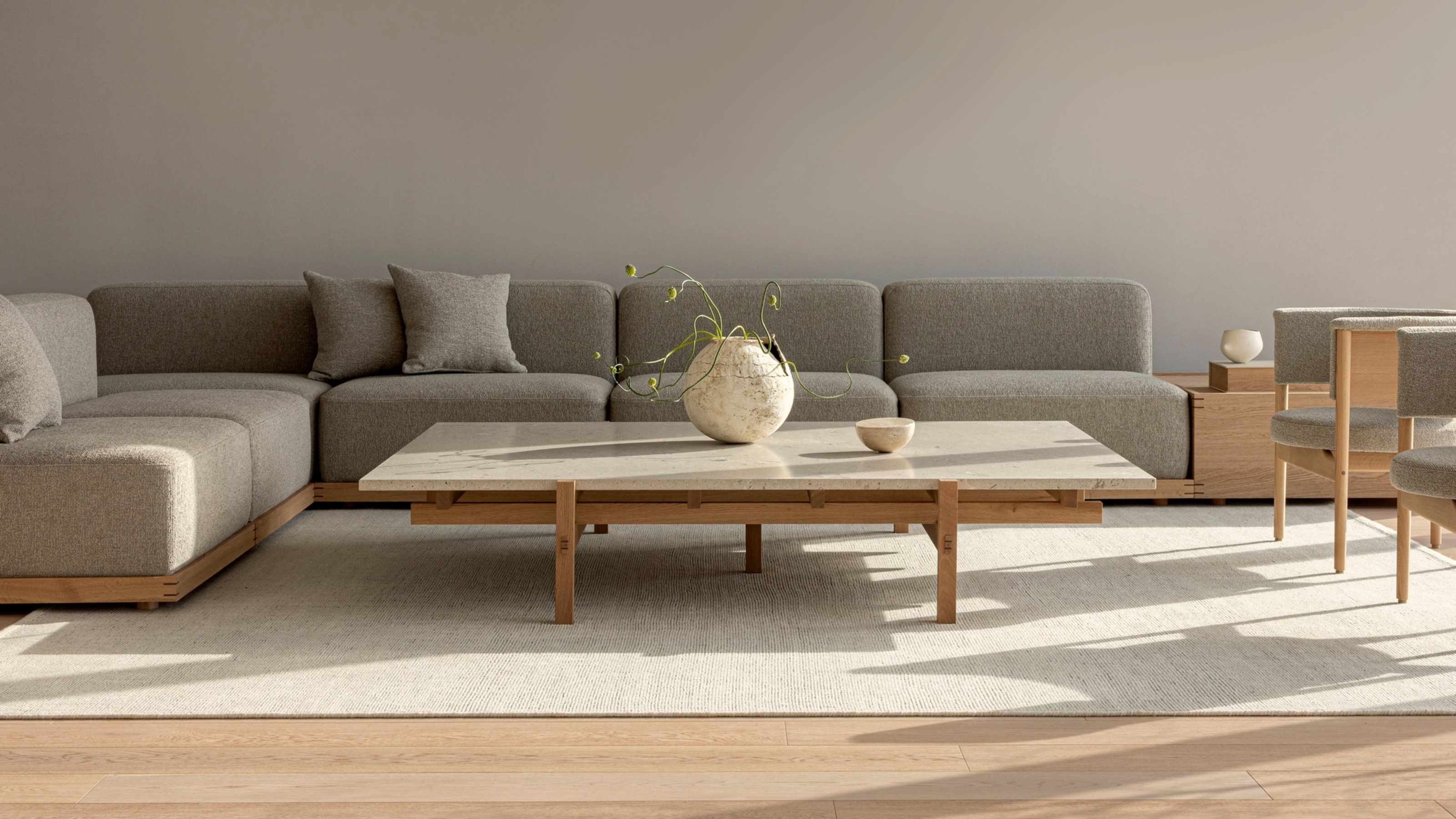 A Scandi living room with a neutral palette, featuring a cream rug, a low profile coffee table, and grey sectional sofa 
