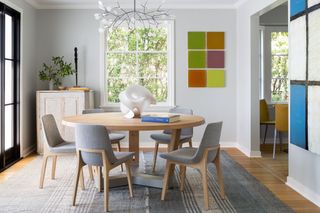 A dining room with a circular wooden table, grey upholstered chairs and multiple large abstract artworks on the walls