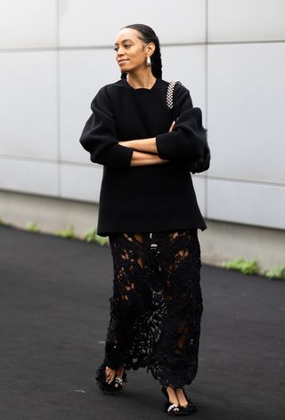 Milan fashion week spring 2025 street style photo of Solange wearing oversized jewelry with a black sweater, sheer black skirt, and black furry heels