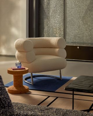 eileen gray's bibendum chair in a room with a cork side table, colorful rug and USM storage in the background