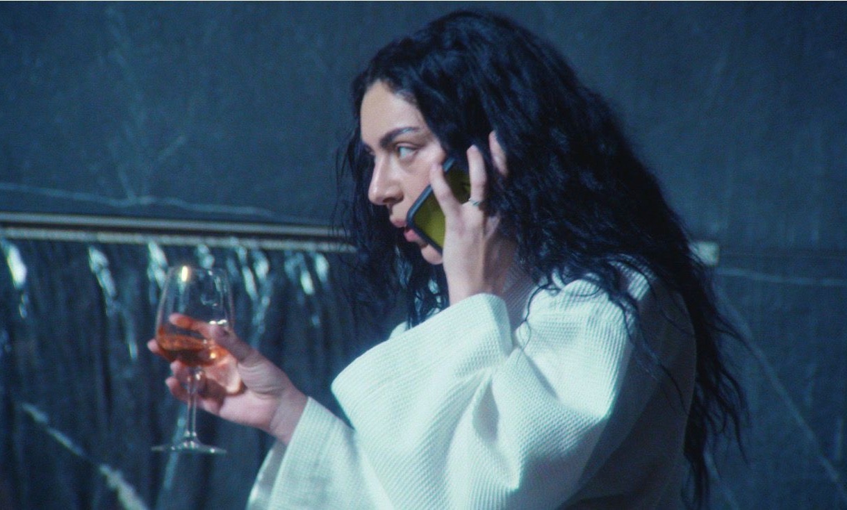 charli xcx speaking on a phone with a brat case and holding a glass of rose in a still from the mockumentary the moment