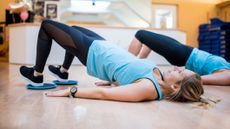 Woman in sportswear on a hard floor lies on her back with her knees bent and heels on sliding discs