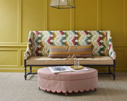 Hallway with painted walls and paneling, colorful upholstered bench with seat cushions, rounded red and white striped ottoman, natural, textured carpet