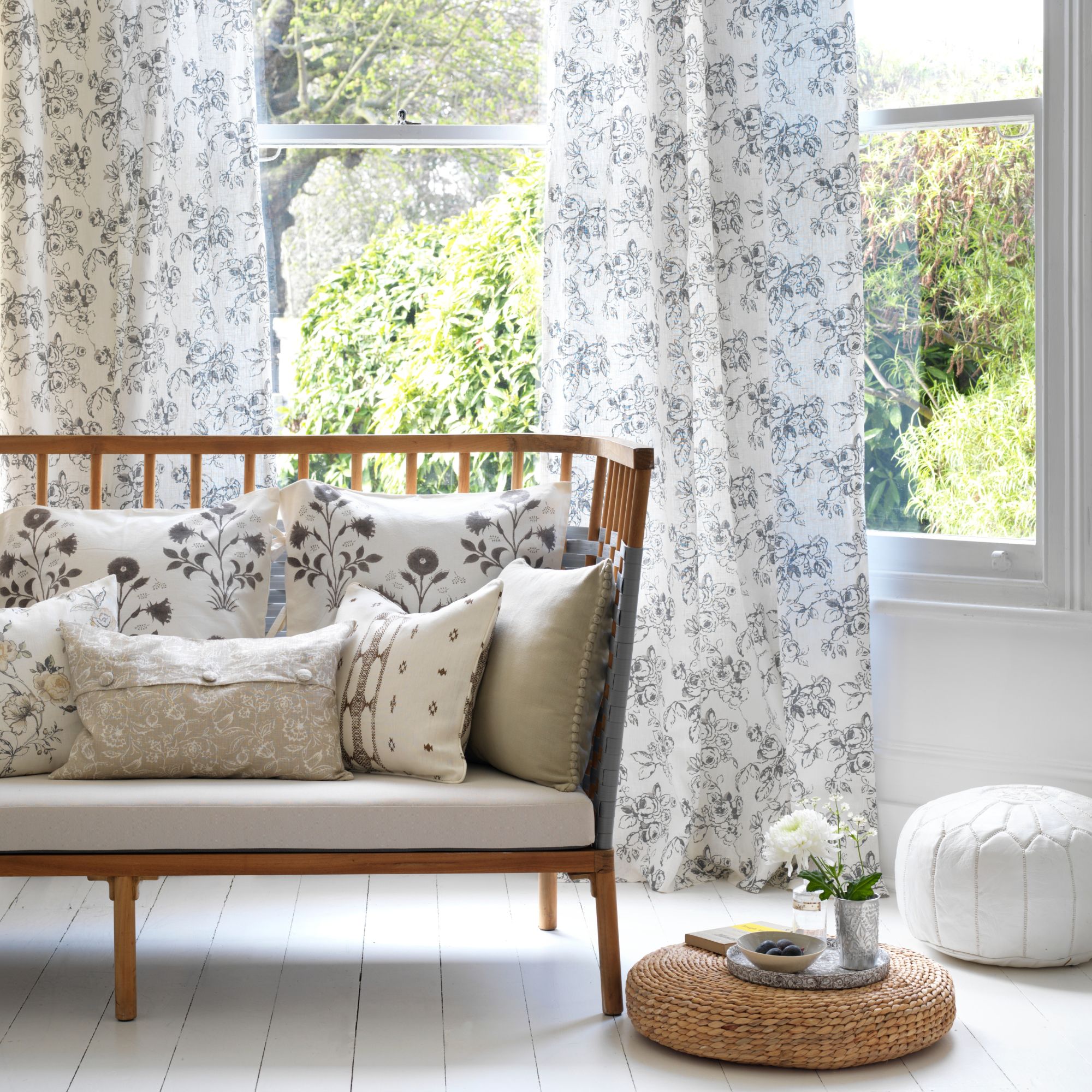 A white sitting area with a wooden bench and rattan tray, with white curtains over the windows