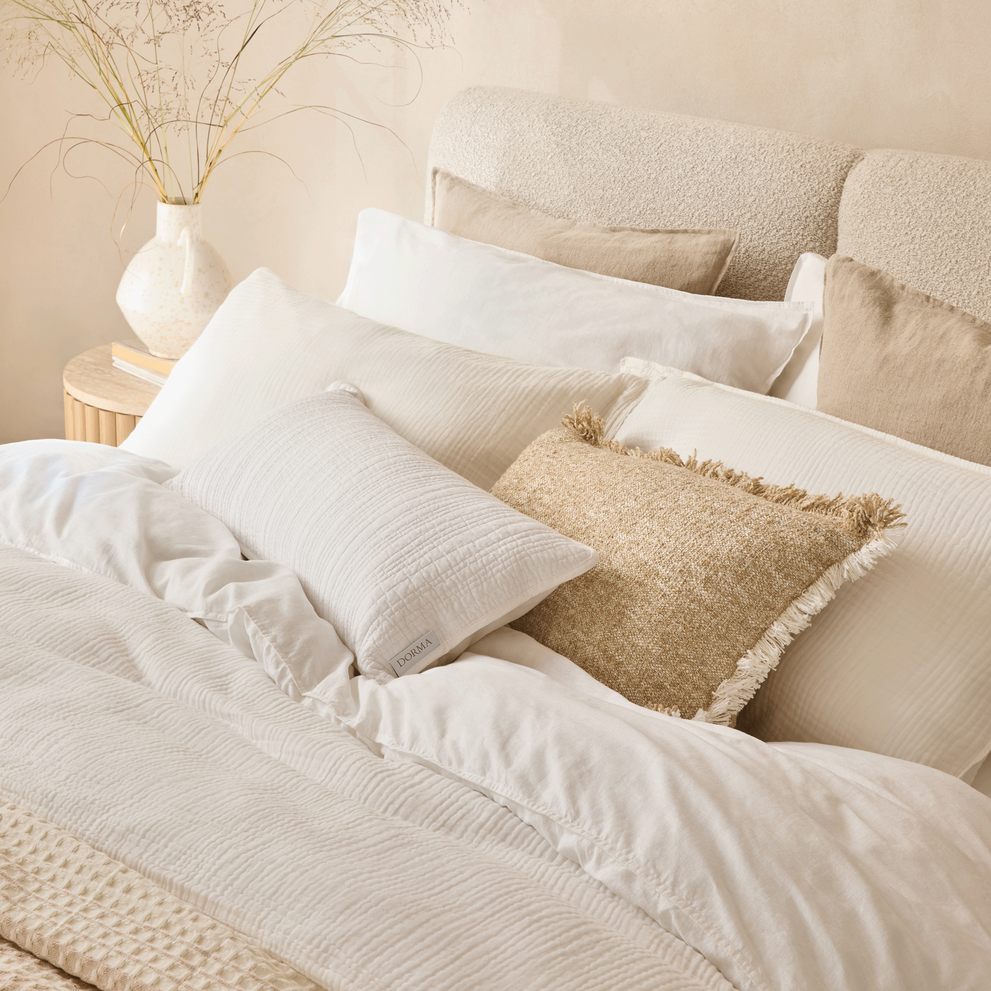 a neutral bedroom with a bed layered in crisp white bedlinen and textured throws and pillows