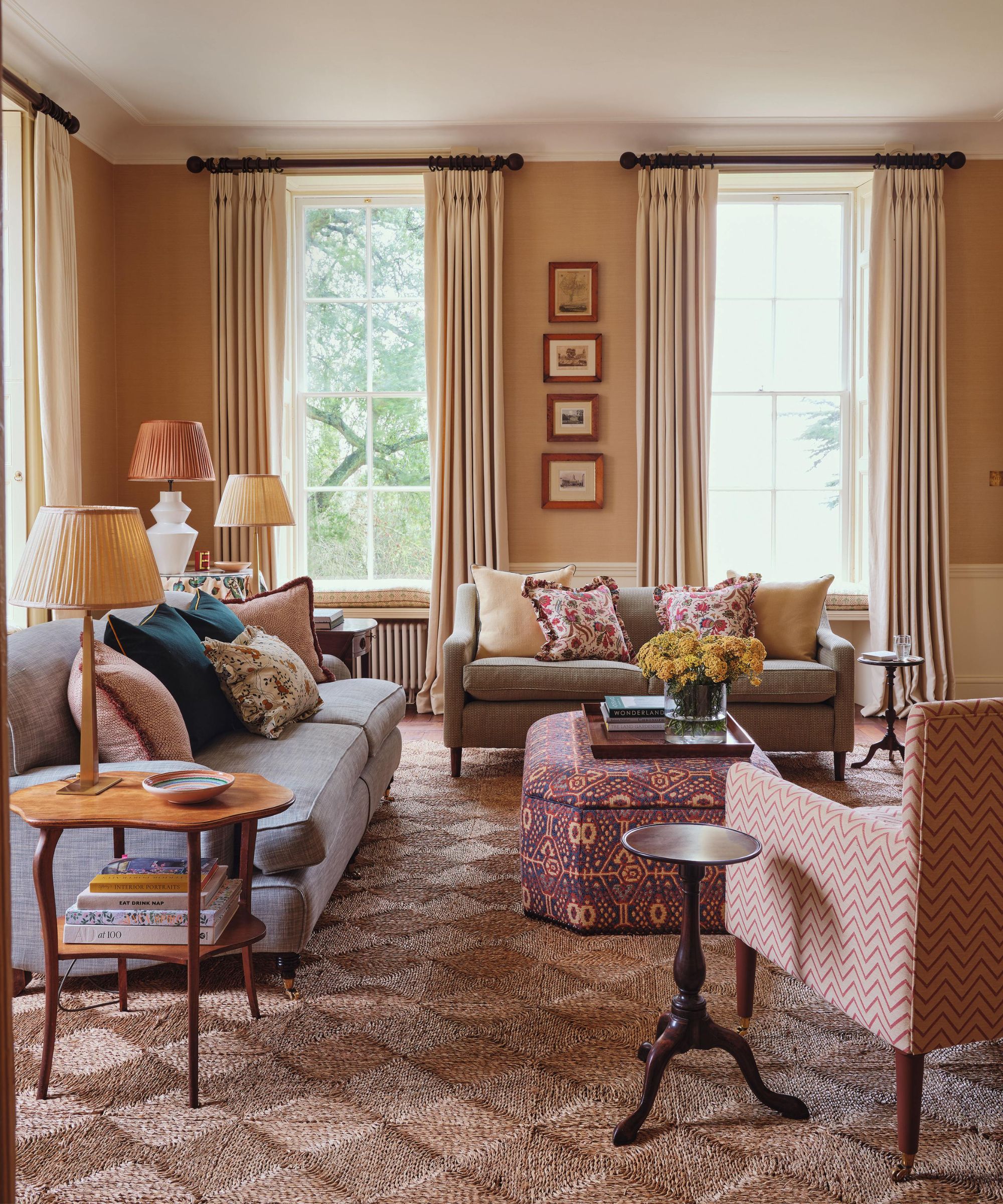 a grasscloth wallpapered living room with a seagrass rug and neutral couches, patterned ottoman and pillows