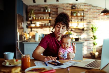 A mother working in the dark on her laptop while her baby sleeps in a stroller.