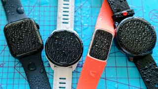 Four smartwatches covered in beads of water.