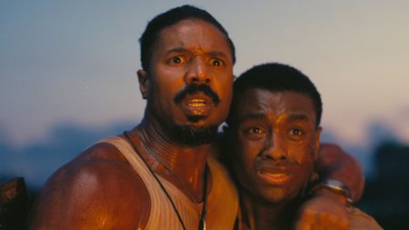 Smoke and Sammie holding each other as they watch a fire burn off-camera in Sinners