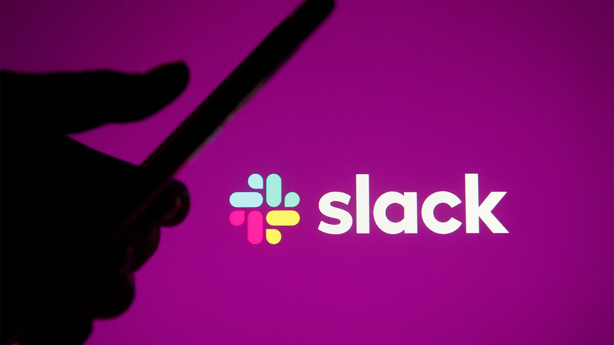 Silhouetted hand using a smartphone pictured in front of the Slack logo and branding.