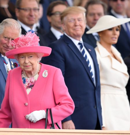 Queen Elizabeth wearing a pink coat and hat walking away from Donald Trump and Melania Trump