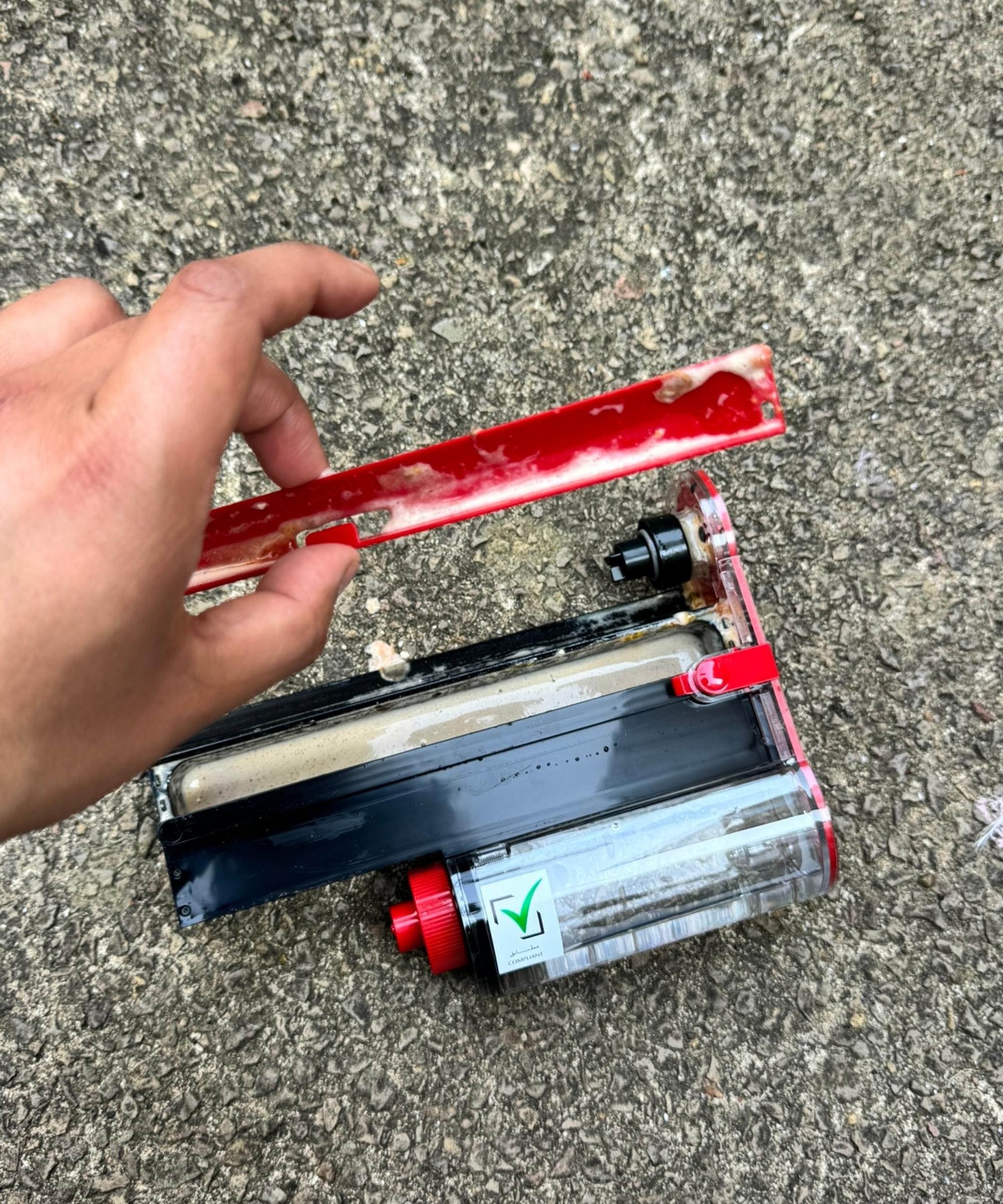 Hand holding one part of a dirty Dyson PencilWash floorhead, above stone floor.