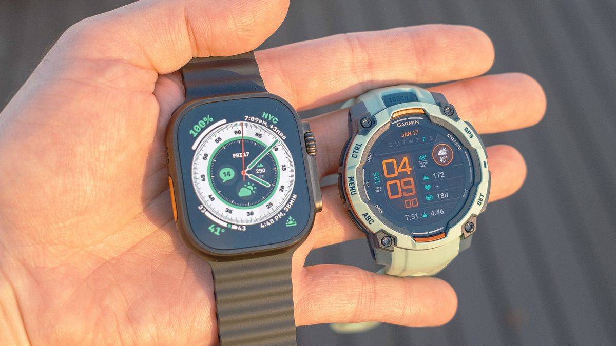 Close-up of the Apple Watch Ultra 2 (left) next to the Garmin Instinct 3 (right) in a user&#039;s hand