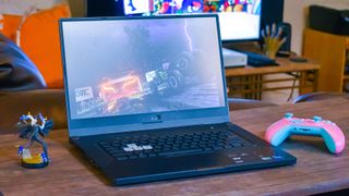 En gaming-laptop av typen Asus TUF Dash F15 står åpen på et skrivebord sammen med en figur og en spillkontroller.