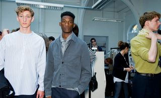 Male models wearing Margaret Howell S/S 2015 collection. On the left the model is wearing a striped white round neck shirt. Next to him the model is wearing a denim jacket and denim pants with his hand in his pocket. On the right the model is wearing a green jersey with a green scarf.