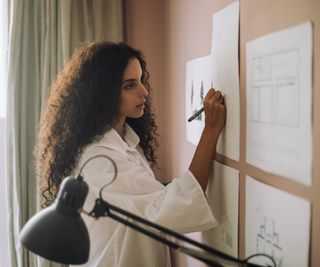 woman stood marking up architectural plans stuck to wall