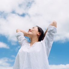 how to work on self love: Low angle portrait of relaxed young woman with her eyes closed, arms outstretched around fresh air and sunlight with head looking up to the blue sky.