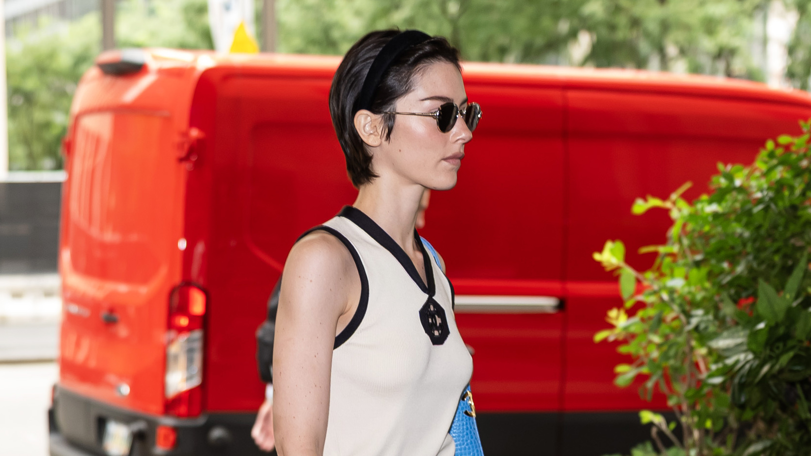 Gracie Abrams wearing a Chanel outfit that includes a cream V-neck tank with black trim, a green logo midi skirt, and a bright blue croc shoulder bag