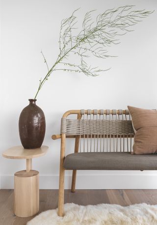 A neutral bench next to a side table with a large vase and sprig of greenery splaying out
