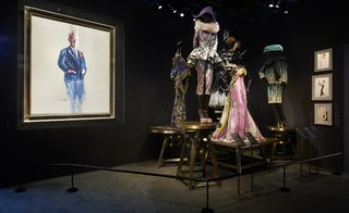 Museum styled room with a portrait on the wall and dresses on mannequins in the middle