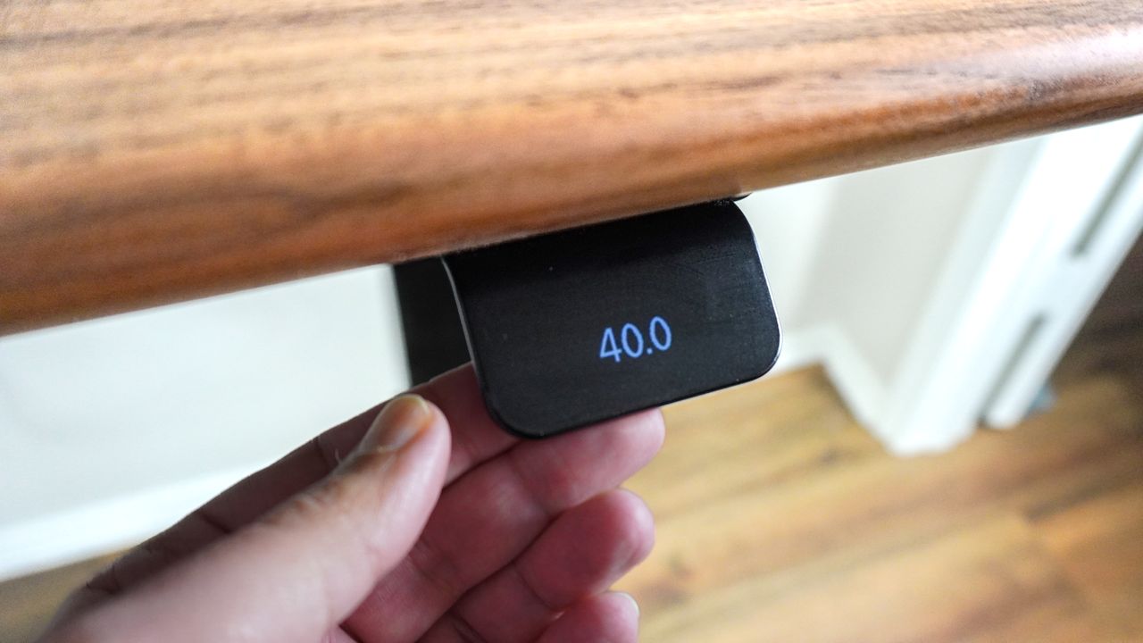 A person adjusting the height of the Oakywood Standing Desk Pro using its paddle-style controller