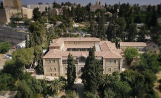 Daytime aerial shot of Hansen house, pale stone building, surrounding tall trees and shrubs, roads, cars, clear sky