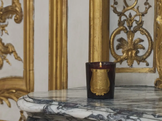 A candle on a marble shelf against a golden-leaf decorated background.