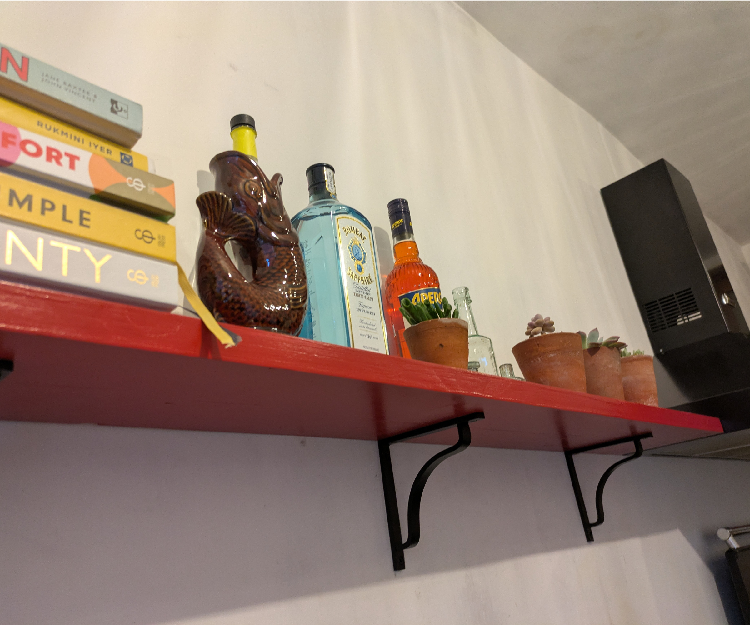 A kitchen shelf laden with cookbooks, ornaments and drinks bottles