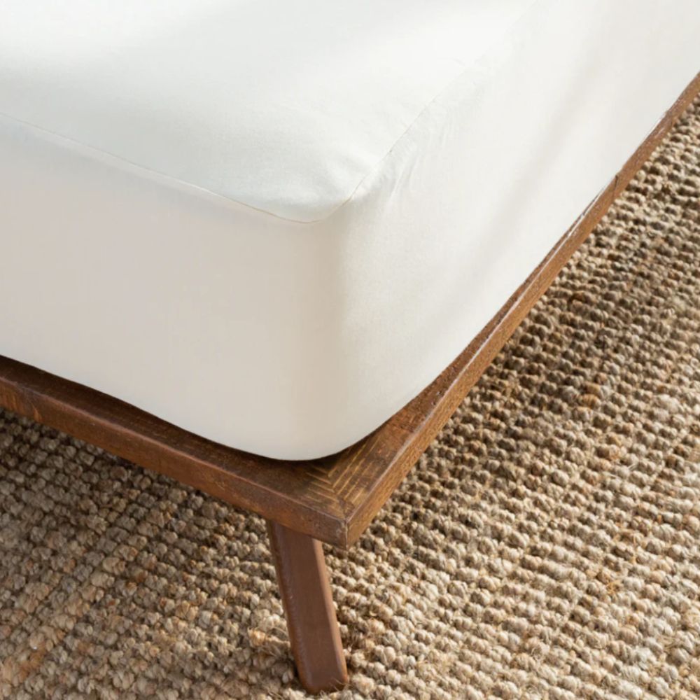 Corner of a wooden bed frame with a mattress protector covering a mattress