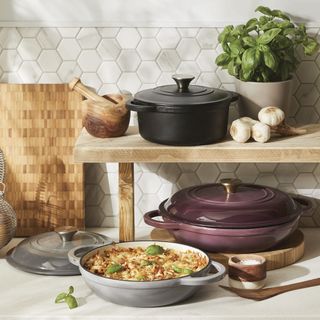 Cast iron cookware in black, grey and plum on a kitchen worktop